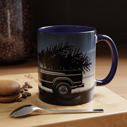 Mug with truck and tree design on a wooden surface with coffee beans and a spoon.