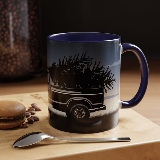 Mug with truck and tree design on a wooden surface with coffee beans and a spoon.